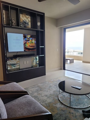 A modern living room with a flat-screen TV mounted on a dark wall, a round glass coffee table, and a sofa. - Villa La Valencia Cabo Luxury 2Bedroom 3Bathroom Suite with Stunning Ocean Views (San José del Cabo)