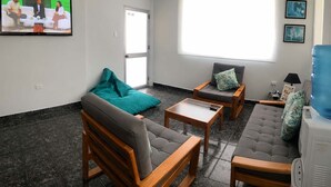 A living room with a sofa, two armchairs, a coffee table, a teal bean bag, a large window, and a television. - Sea View | Hot Tub | Steps to Beach (Atacames)