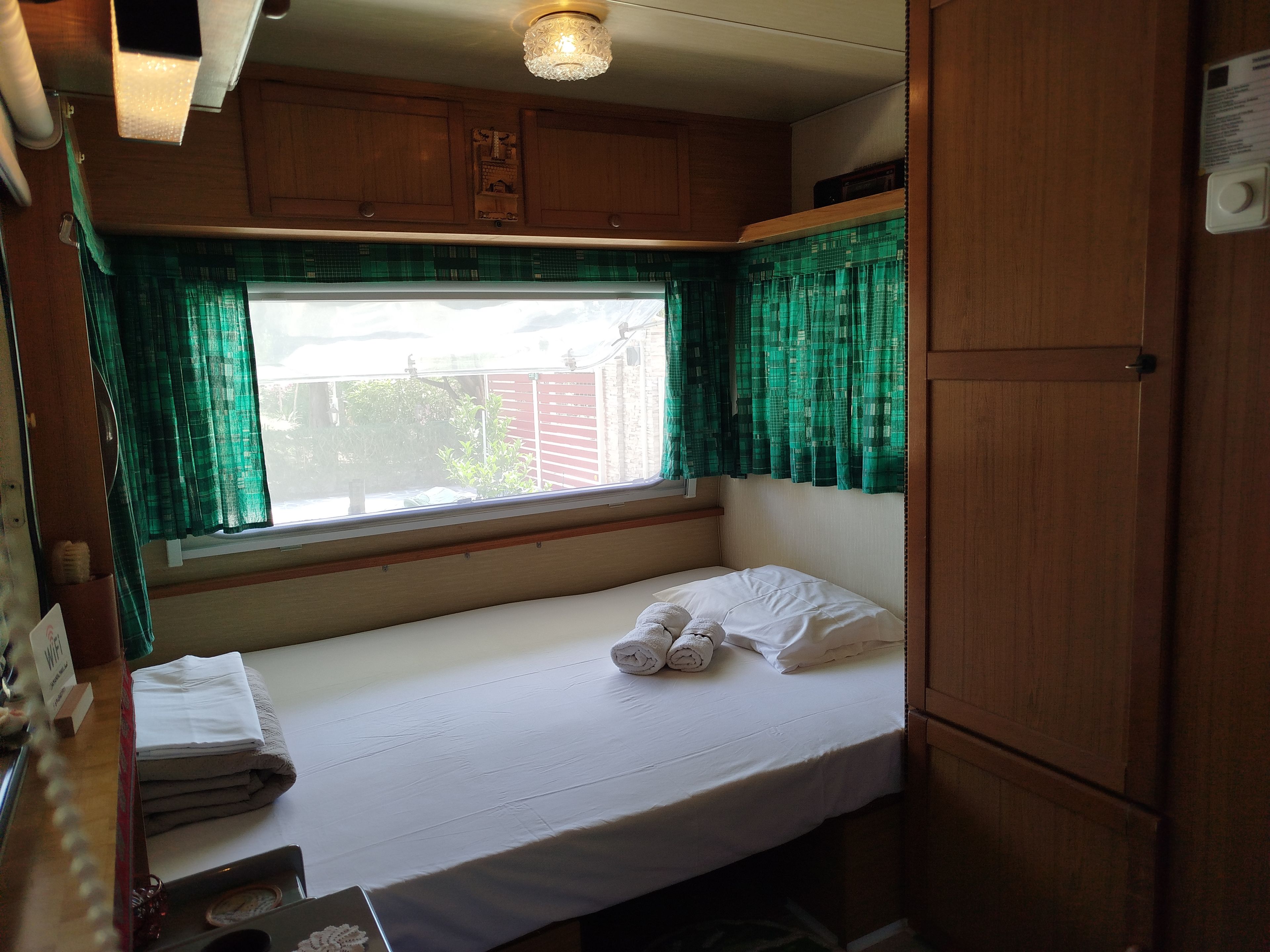 Une petite chambre avec un lit simple, une fenêtre, des armoires en bois et un lit recouvert de draps blancs.