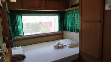 Une petite chambre avec un lit simple, une fenêtre, des armoires en bois et un lit recouvert de draps blancs.