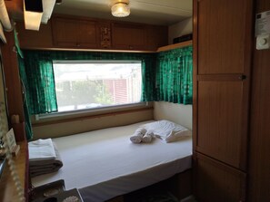 A small, single-bed room with a window, wooden cabinets, and a bed with white bedding.