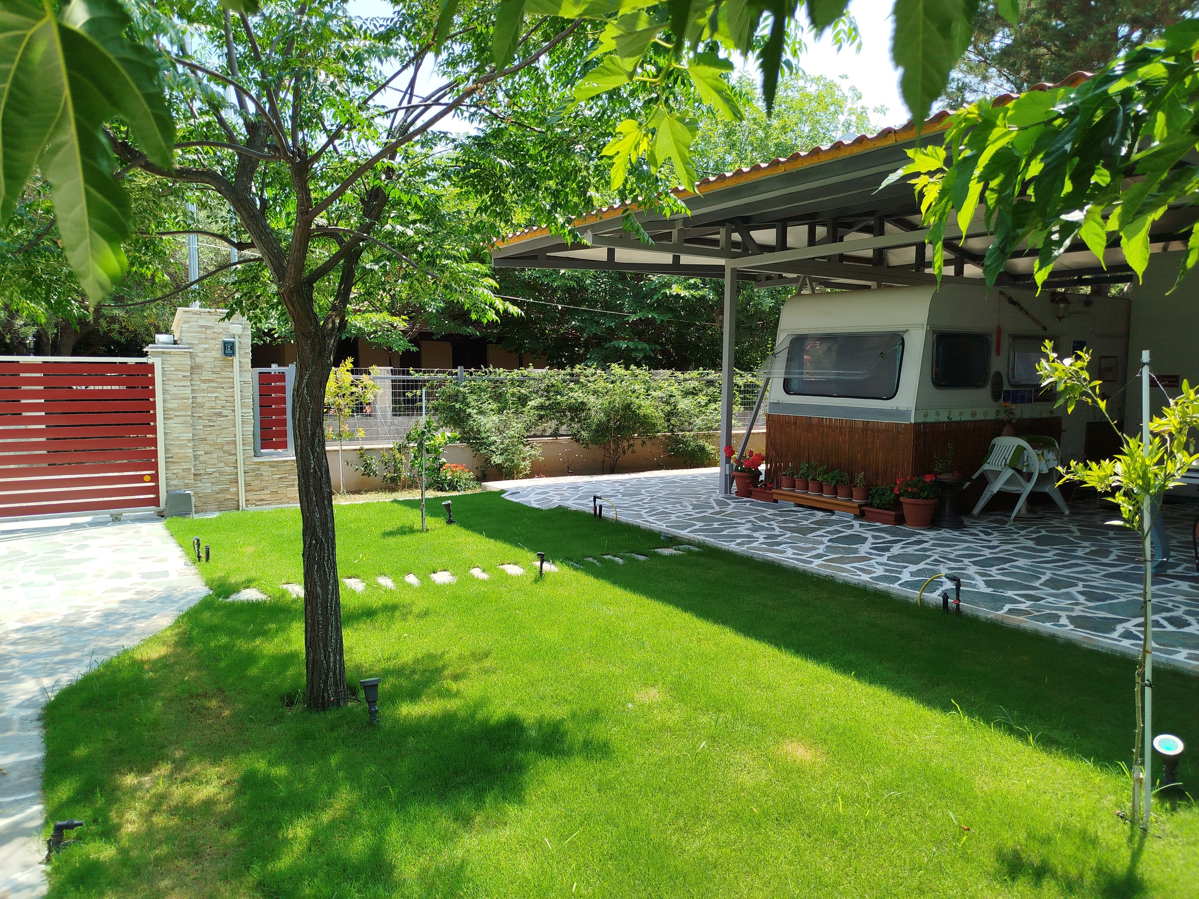 Jardí ben cuidat amb un pati pavimentat, una zona d'estar coberta i un vehicle a dins.
