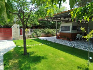 Un jardin bien entretenu, avec une terrasse dallée, un espace salon abrité et un véhicule garé à l’intérieur.