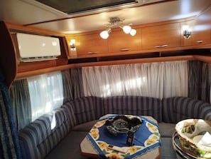 Un interior de autocaravana acogedor, con zona de estar, una mesa y un plato decorativo, además de un ventilador de techo.