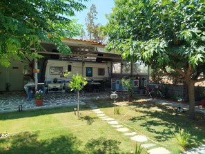 Un barrio residencial con una casa, una furgoneta estacionada y un jardín con césped, plantas en macetas y un árbol.
