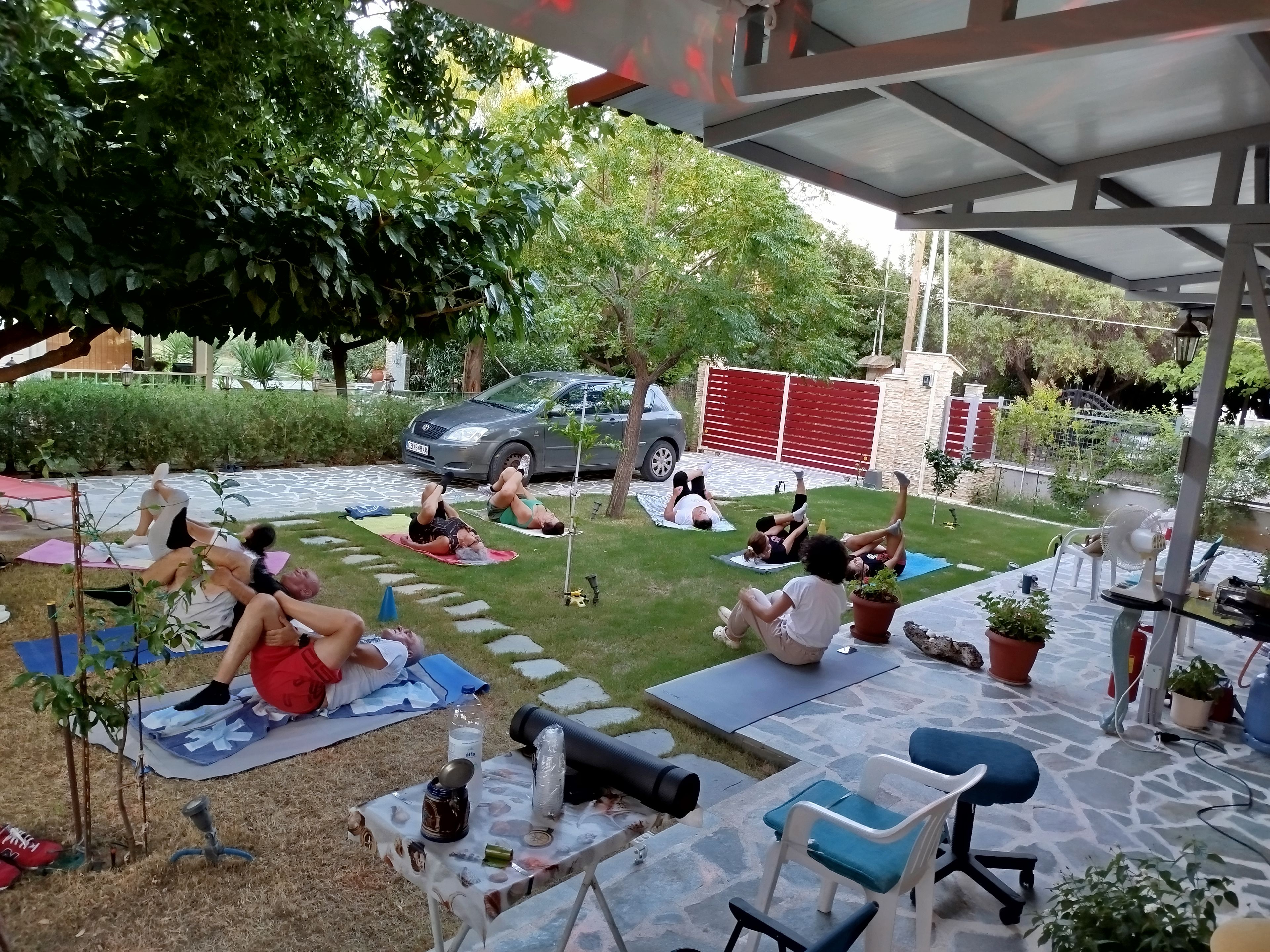 An outdoor patio area with people lying on mats, a car, and a red gate in the background.