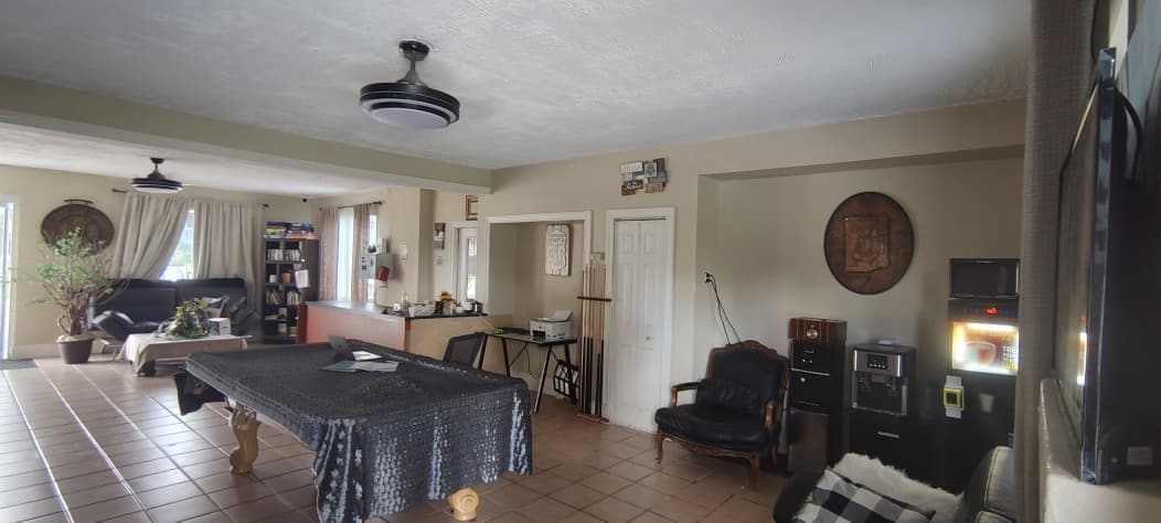 Amplia sala de estar con una mesa de comedor, un sofá y una silla. Se observa una zona de cocina al fondo.