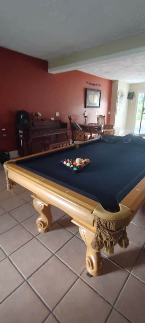 A pool table with balls, a wooden piano, and a framed picture on the wall.