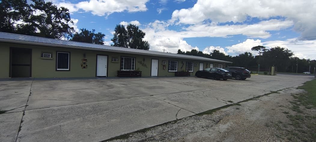A motel with a row of rooms, a parking area, and a building with a flat roof.