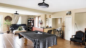 A spacious living room with a large table, a black leather sofa, a bookshelf, and a dining area.