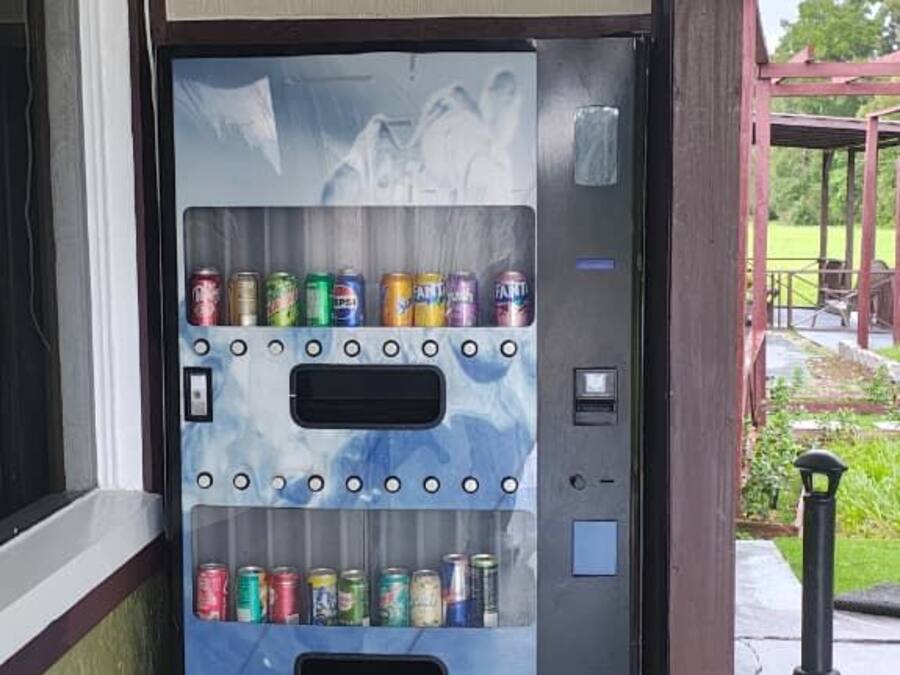 A vending machine with multiple beverage options, located outdoors near a building entrance.