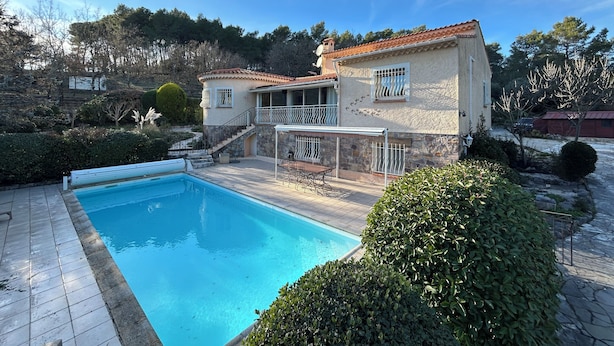 Et poolområde med et klart, blåt pool, en sti af sten og en bygning med balkon.