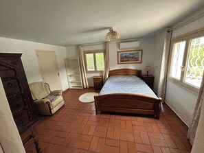 Ein Schlafzimmer mit einem hölzernen Bett, einem Sessel, einem Kleiderschrank, einem Nachttisch und einem Fenster mit Vorhängen.