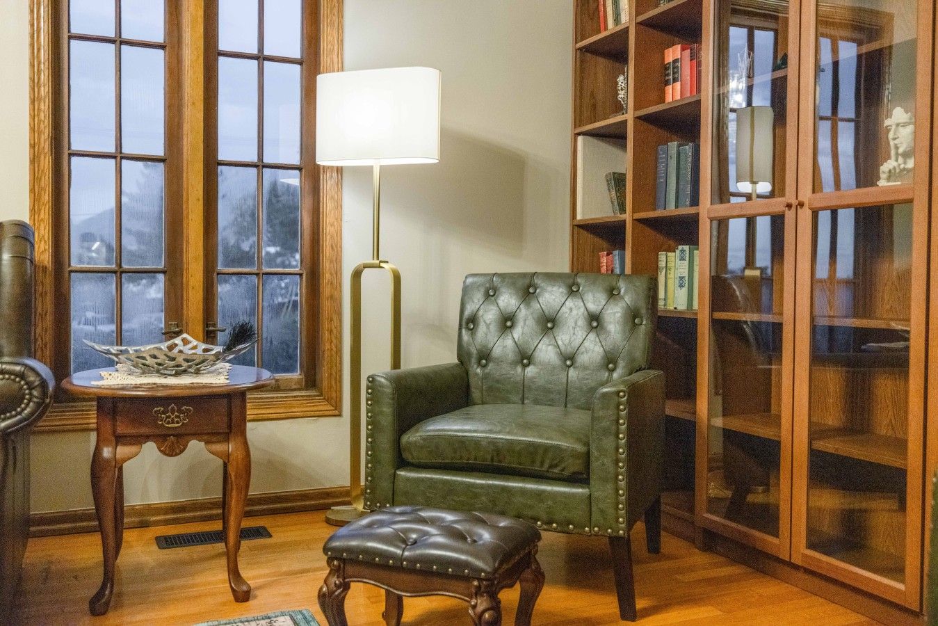 Une pièce comprenant un fauteuil en cuir vert, une table d’appoint en bois avec une lampe et une bibliothèque remplie de livres.