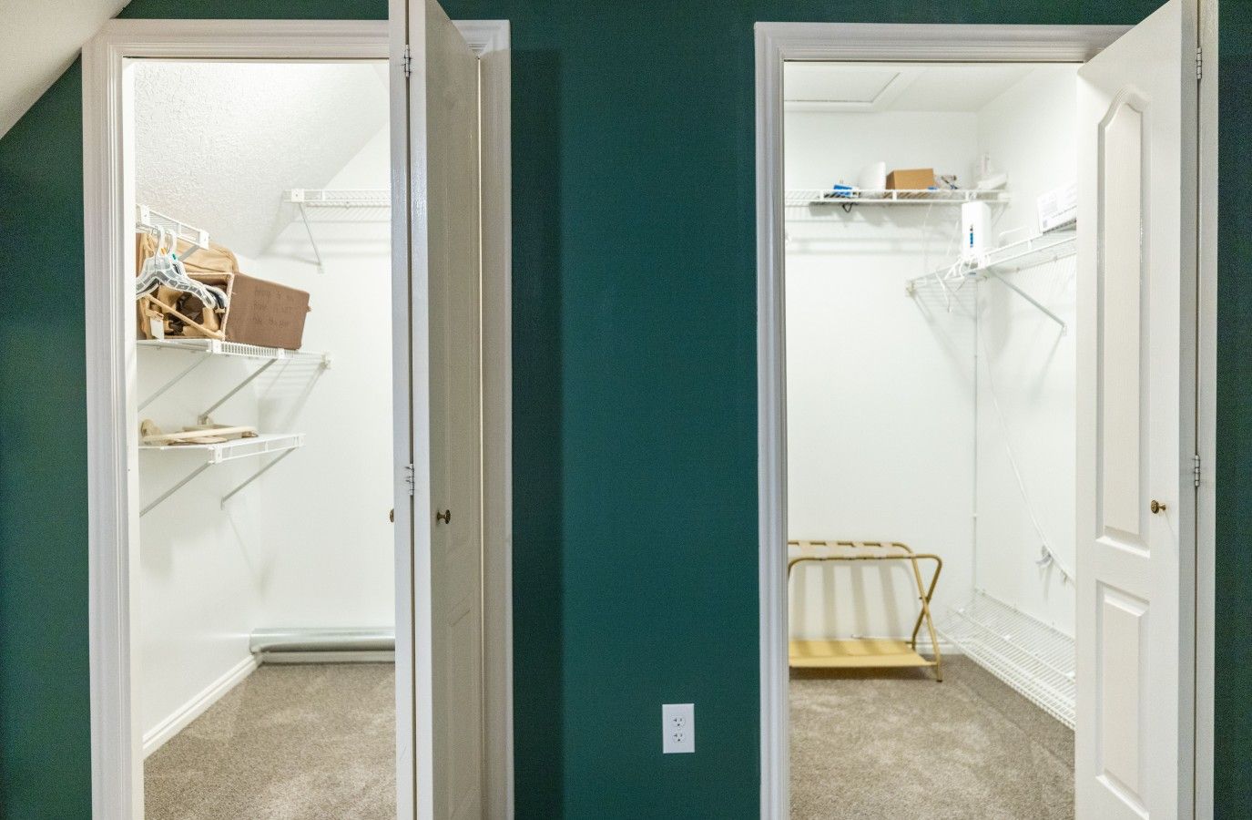 Habitación con armario que incluye estantes y espacio para colgar, piso alfombrado y una puerta que da a otra habitación.
