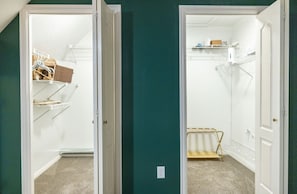Habitació amb un armari que conté prestatges i espai per penjar roba, sòl amb moqueta i una porta que dona a una altra habitació.