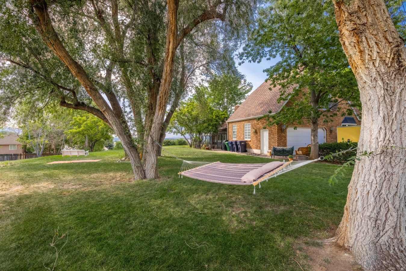 Une cour arrière verdoyante avec un hamac, un arbre et une maison dotée d’un garage.
