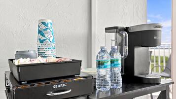 Una cafetera Keurig, dos botellas de agua, una pila de vasos y un cubo de basura sobre una mesa.