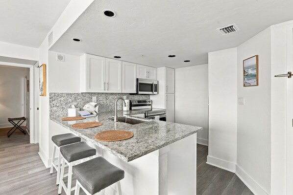 A modern kitchen with white cabinets, a granite countertop, and a built-in oven.