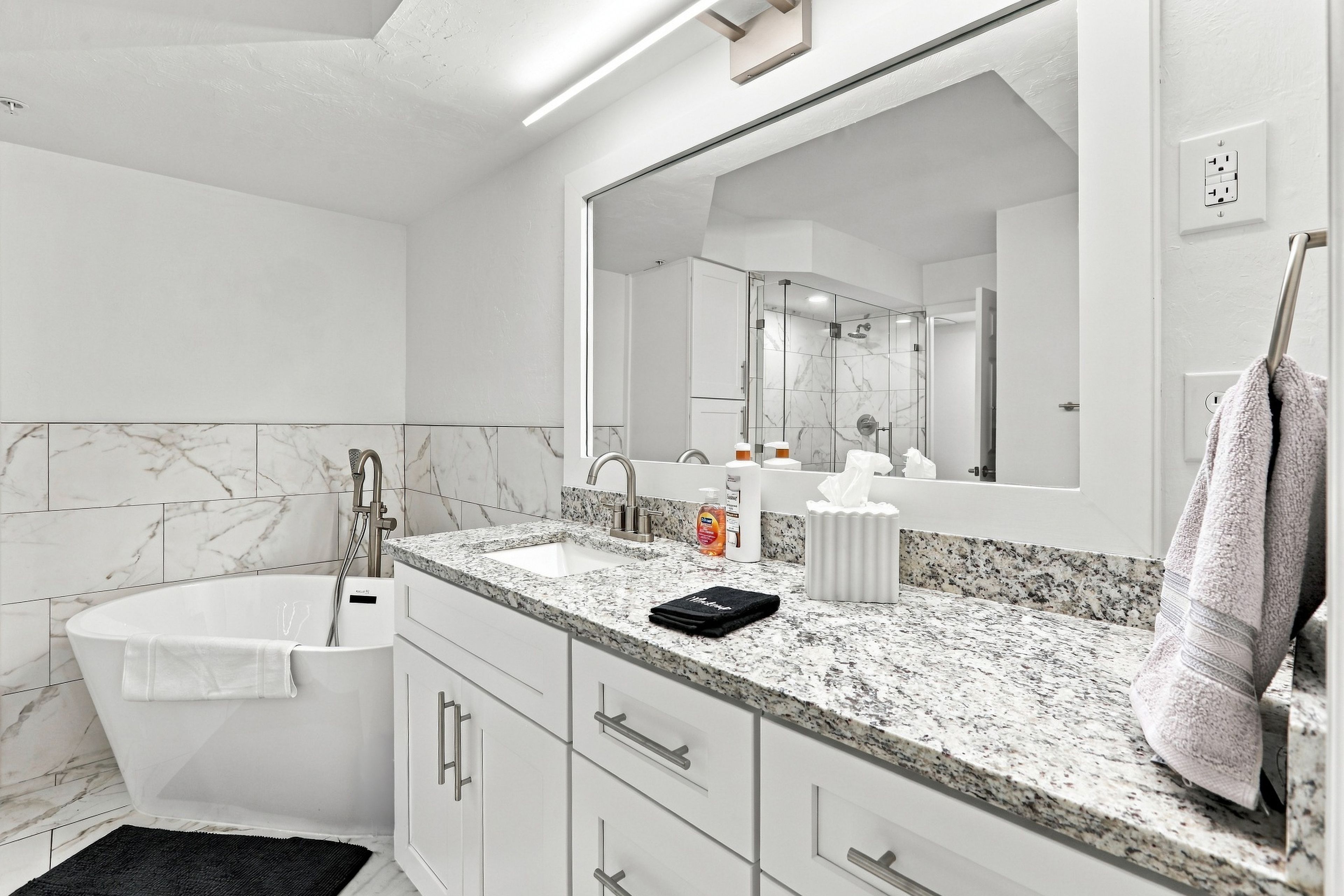 Un baño moderno con una bañera independiente, un espejo grande y una encimera de granito.
