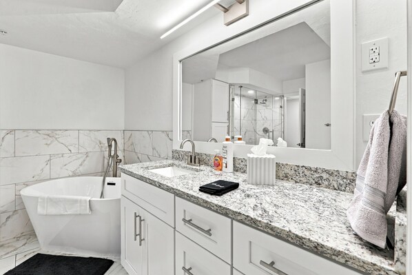 A modern bathroom with a freestanding bathtub, a large mirror, and a granite countertop.