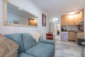A living room with a sofa, a dining table with chairs, a kitchen area with cabinets and appliances, and a large mirror on the wall. - Beach days & tapas nights in the heart of Fuengirola (Fuengirola)