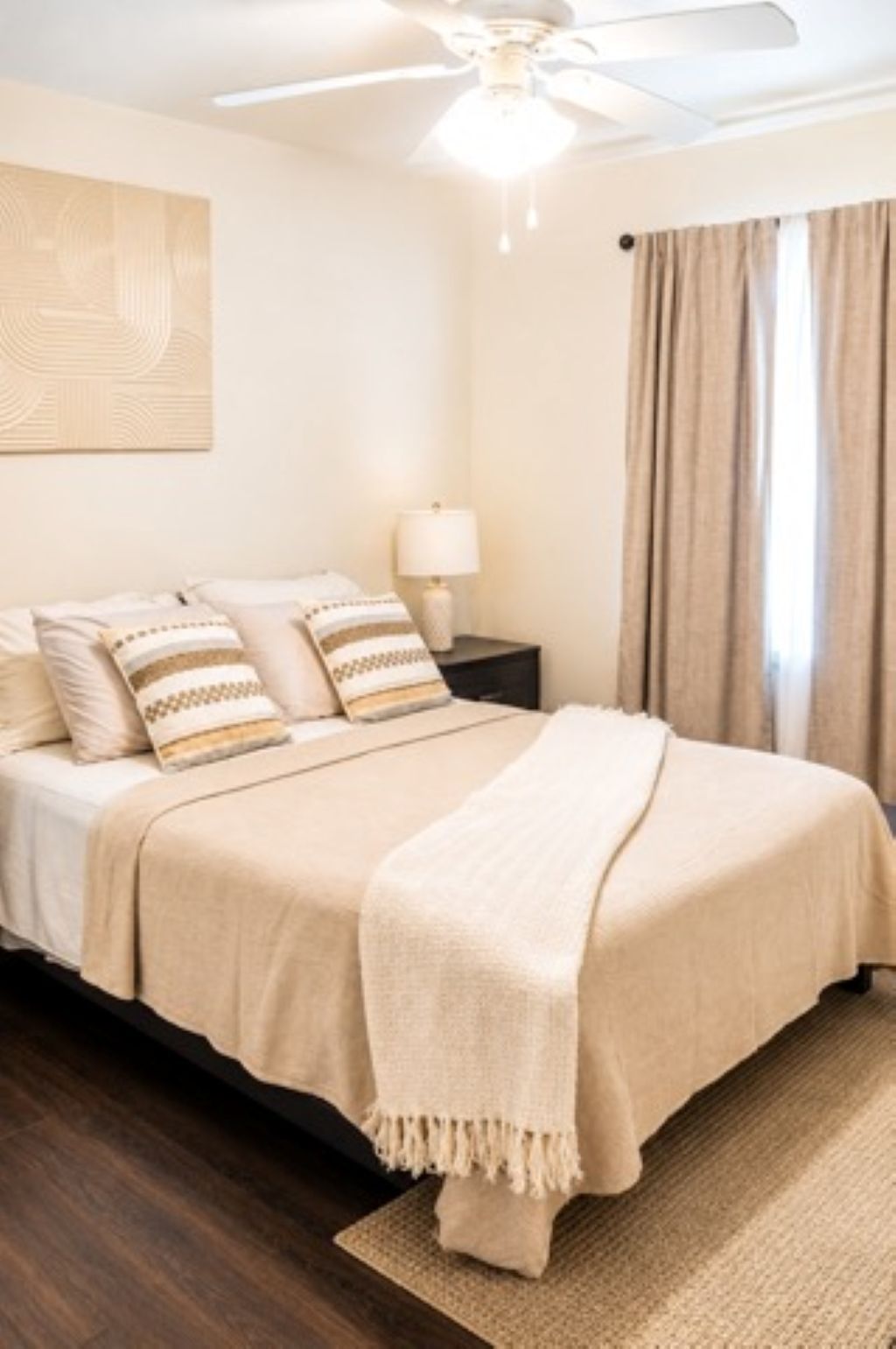 A bedroom with a bed, a nightstand, a lamp, a ceiling fan, and a window with curtains.