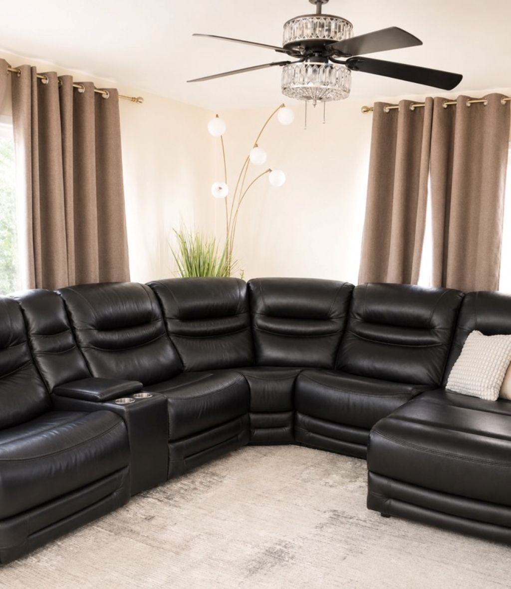 A black leather sectional sofa with a built-in coffee table and side tables, a crystal chandelier, and a ceiling fan.