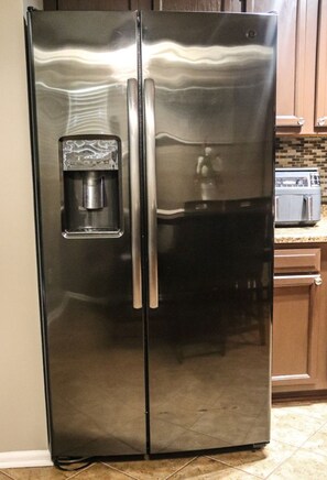 A stainless steel refrigerator with a water dispenser, located in a kitchen with wooden cabinets and a tiled floor.