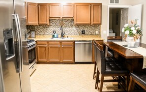 Una cocina con armarios de madera, un refrigerador de acero inoxidable, un lavavajillas y un comedor con mesa y sillas.