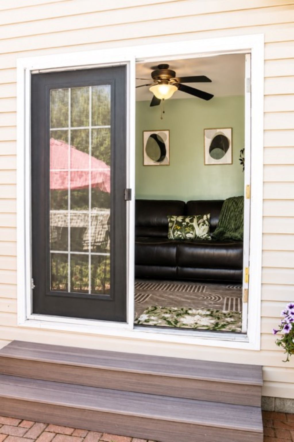 A sliding glass door leading to a living room with a ceiling fan, a dark leather couch, and a patterned rug.