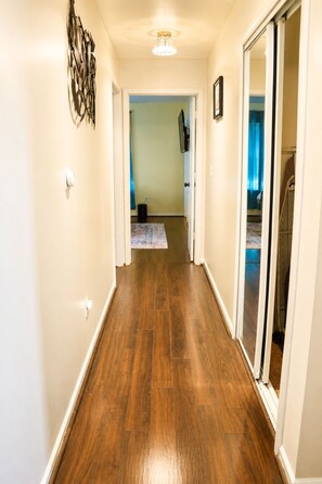 Ein Flur mit Holzboden, einer Deckenleuchte und einer Tür zu einem weiteren Zimmer.