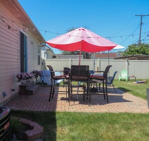 A patio with a table and chairs under a red umbrella, a grill, and a flower pot.