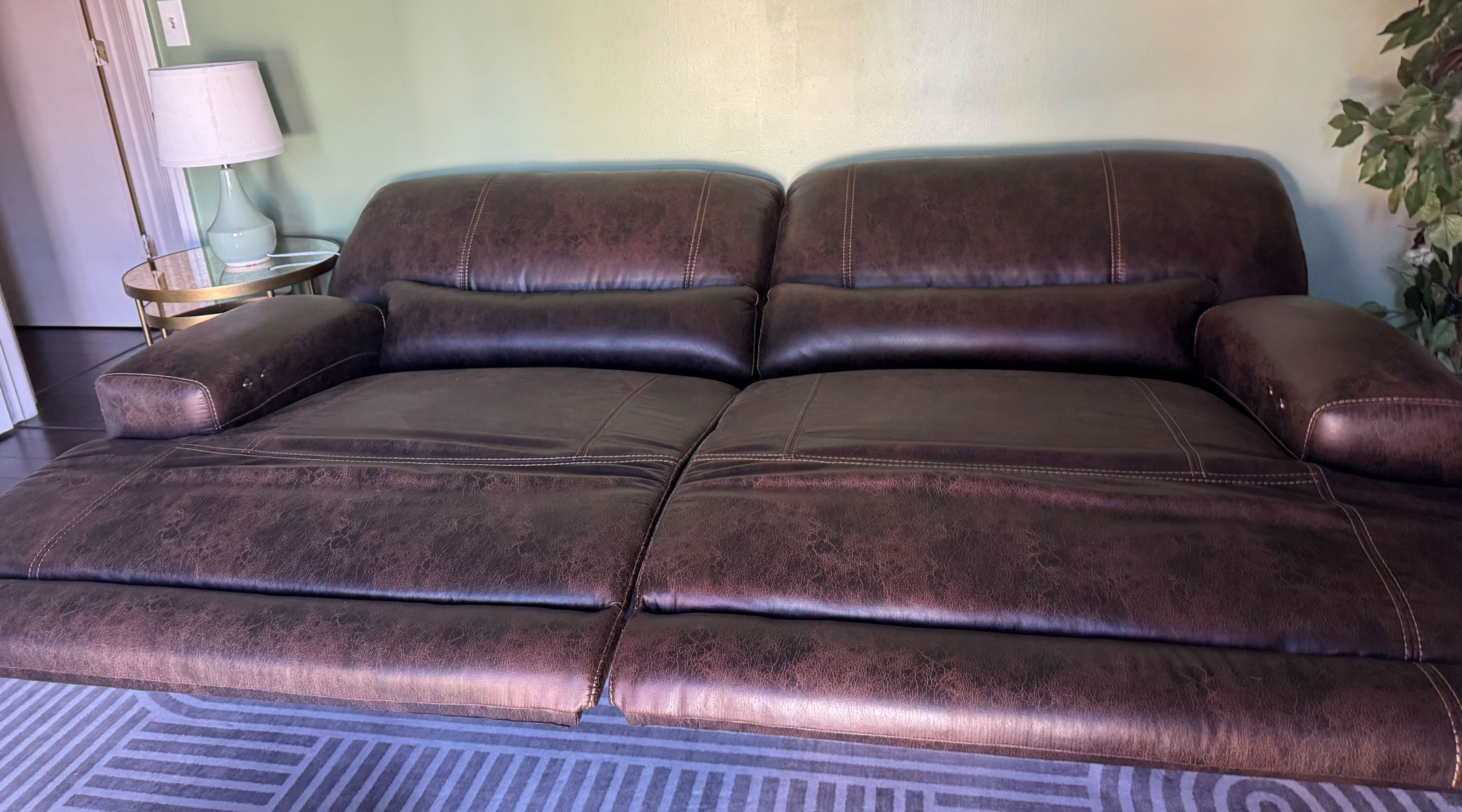 A brown leather sofa with a patterned rug in a room with a lamp and a plant.
