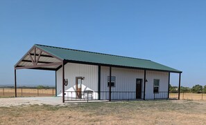 A single-story building with a green roof, a covered porch, and a fenced area.