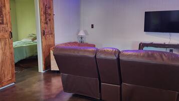 A room with a large brown leather sofa, a sliding barn door, a flat-screen TV, and a neon sign reading 'Rockin' Race-Stays'.