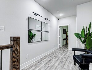 A hallway with a wooden railing, a black bench, and a potted plant. - Luxury Modern Stay Minutes from NRG & Med Center (Houston)
