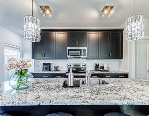 A modern kitchen with dark cabinets, stainless steel appliances, a marble countertop, and pendant lights. - Luxury Modern Stay Minutes from NRG & Med Center (Houston)