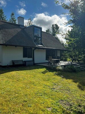Ein Haus mit einem Strohdach, einem Schornstein und einer Terrasse mit Gartenmöbeln.