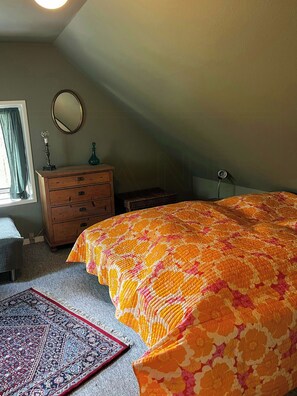 Ein Schlafzimmer mit einem großen Bett, einem Schminktisch, einem Spiegel und einem Fenster mit Vorhängen.