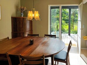 A dining area with a wooden table and chairs, a cabinet, and a view of a garden through a glass door. - Thatched holiday home in nature by the Gudenå (Ans)