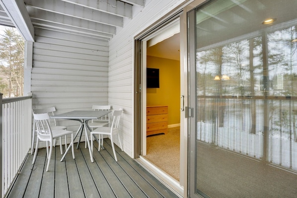 A covered outdoor area with a table and chairs, a sliding glass door leading to an interior room with a dresser and a television.