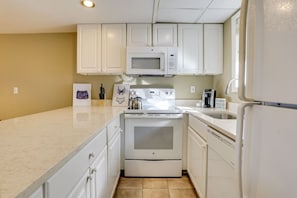 A kitchen with white cabinets, a microwave, a stove, and a sink.