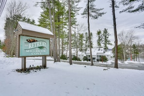 A sign for The Retreat at Millbrook Cove with a snowy landscape and trees in the background.