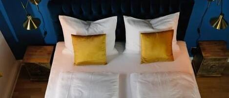 A bed with white linens, two yellow pillows, and a blue headboard.