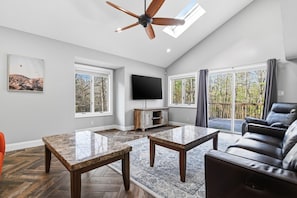 A spacious living room with a ceiling fan, a flat-screen TV, a fireplace, and a large window overlooking a deck. - Fairview House 2.5 hours from NYC & PHL (Tafton)
