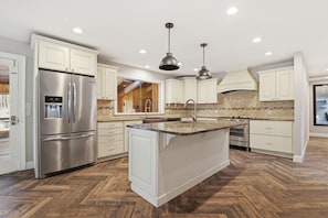 A modern kitchen with a stainless steel refrigerator, white cabinetry, a herringbone wood floor, and pendant lighting. - Fairview House 2.5 hours from NYC & PHL (Tafton)