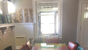 Un comedor con una mesa de vidrio, sillas coloridas, chimenea y ventilador de techo.