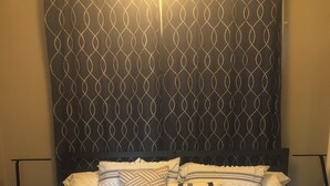 Una cama con cabecera estampada, varios almohadones y colcha a rayas.
