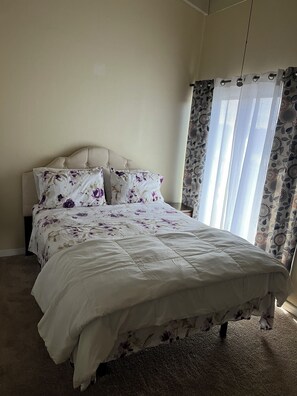 A bedroom with a bed, a headboard, and a window with curtains.